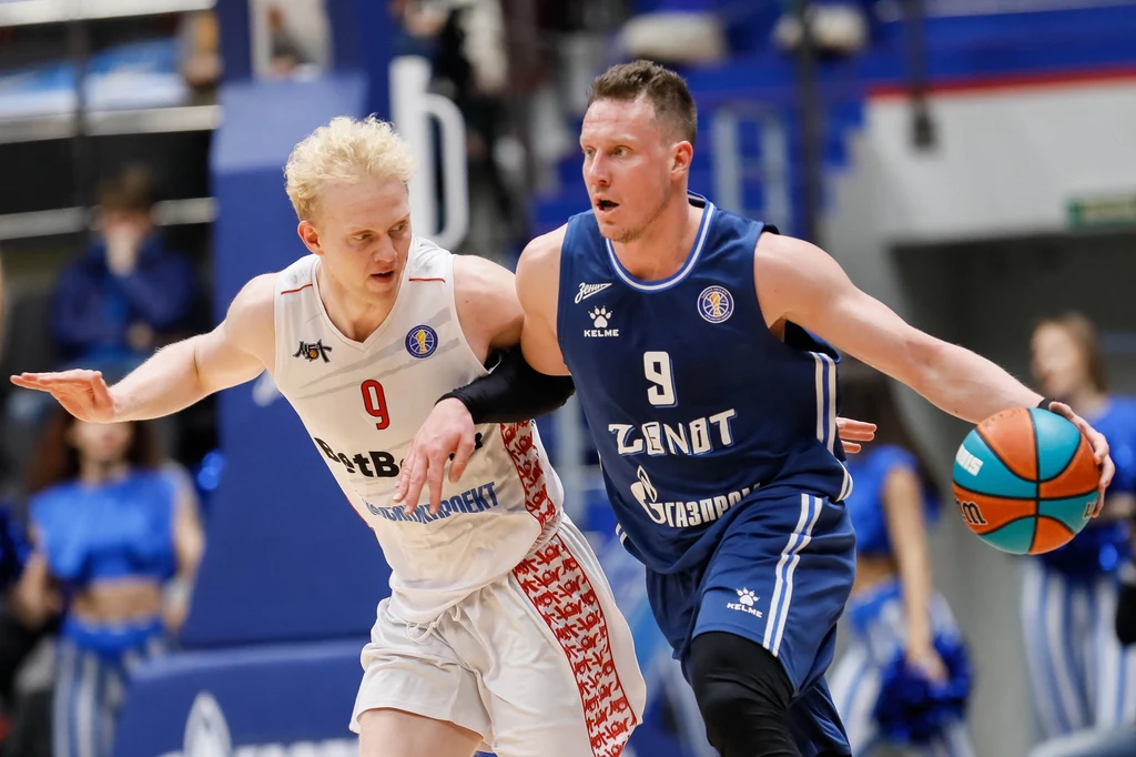 Daniił Kasatkin znalazł się w poważnych tarapatach. Amerykanie obserwowali go od dłuższego czasu Dwóch zawodników rywalizuje podczas intensywnego meczu koszykówki, jeden ubrany w biały, drugi w niebieski strój, trzymający piłkę, pozostali zawodnicy i kibice w tle są zamazani.