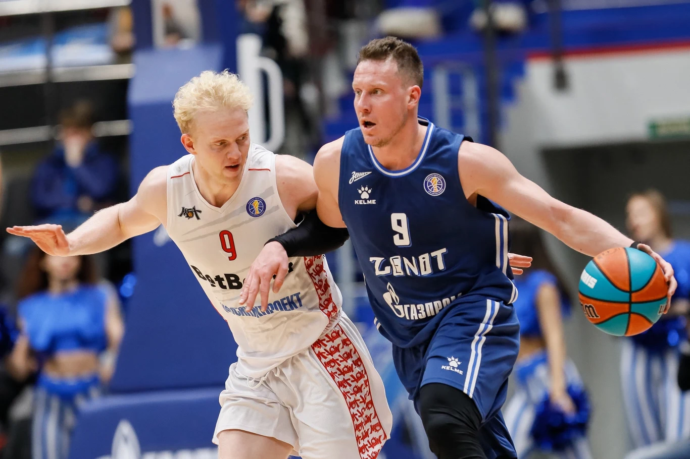 Daniił Kasatkin znalazł się w poważnych tarapatach. Amerykanie obserwowali go od dłuższego czasu Dwóch zawodników rywalizuje podczas intensywnego meczu koszykówki, jeden ubrany w biały, drugi w niebieski strój, trzymający piłkę, pozostali zawodnicy i kibice w tle są zamazani.