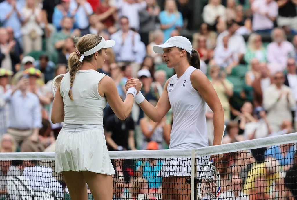 Wimbledon 2025 / Day 6 / Swiatek vs Collins Dwie tenisistki w białych strojach ściskają sobie ręce na środku kortu, za siatką, po zakończonym meczu, w tle widoczni kibice na trybunach.