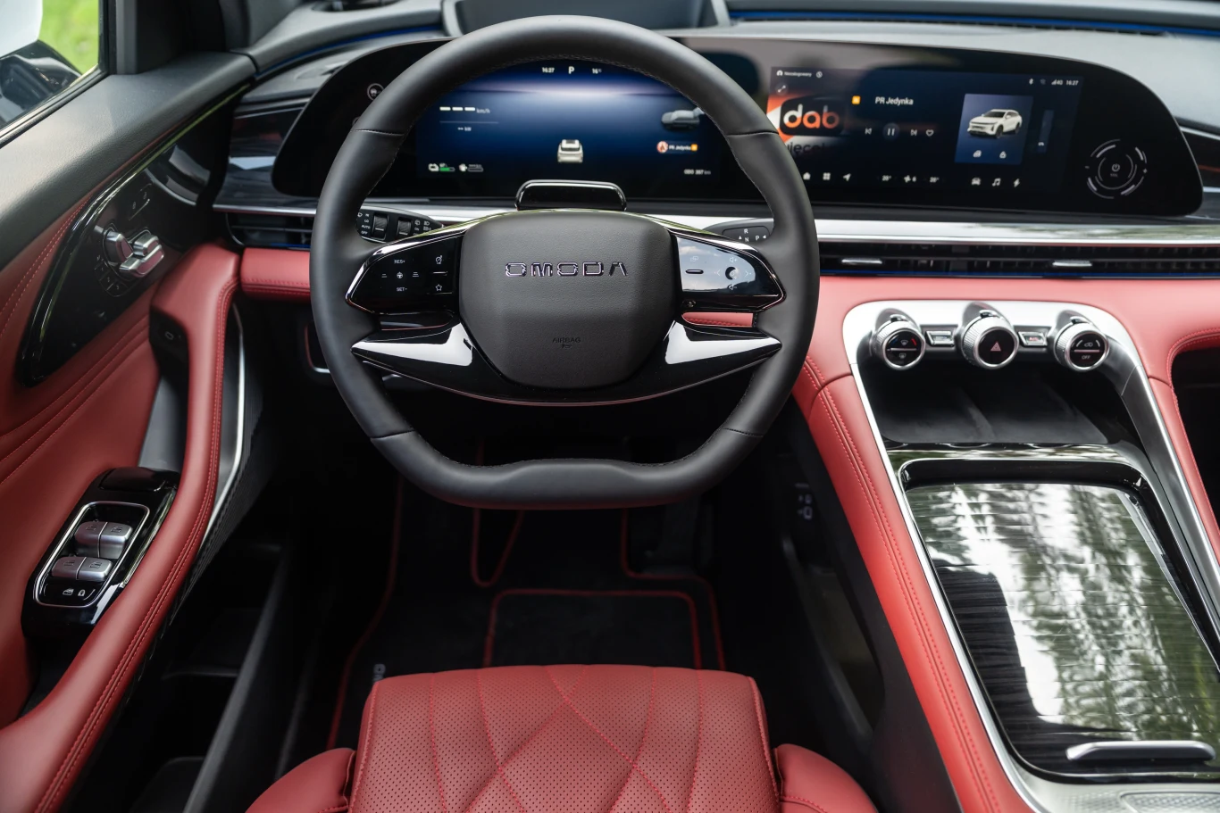 Nowoczesne wnętrze samochodu z luksusowym, czerwonym wykończeniem, dużym elektronicznym wyświetlaczem na desce rozdzielczej i elegancką kierownicą.
