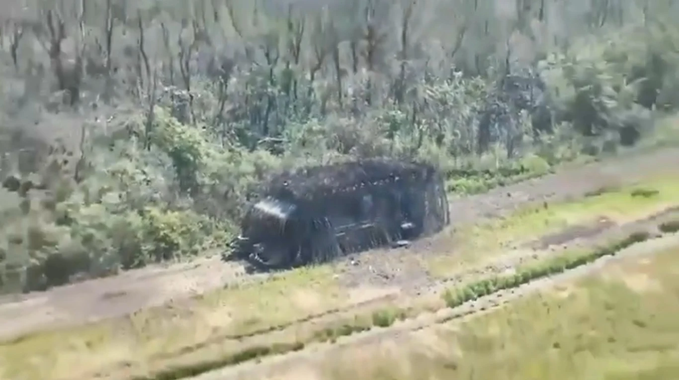 Ukraińska armia uderzyła aż 60 dronami w rosyjski pancerny pojazd Pojazd wojskowy zakamuflowany gałęziami i siatką maskującą stoi na polnej drodze w pobliżu zalesionego terenu, otoczenie stanowią trawa i krzewy.