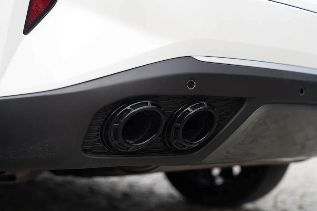Cztery okrągłe końcówki wydechu w kolorze czarnym bardzo przypominają opcjonalny sportowy wydech w Porsche Cayenne. Niestety to tylko atrapy Podwójny wydech samochodowy umieszczony w tylnym zderzaku białego auta, detale otoczenia i elementów pojazdu widoczne w zbliżeniu.