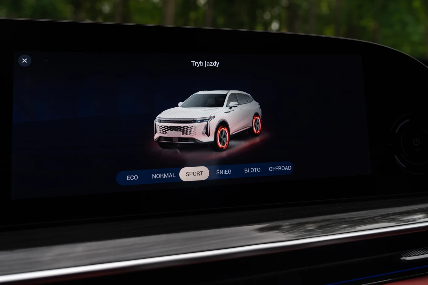 Ekran systemu multimedialnego samochodu z wirtualnym obrazem SUV-a i zaznaczoną opcją trybu jazdy SPORT, menu wyboru dostępnych trybów znajduje się na dole ekranu.