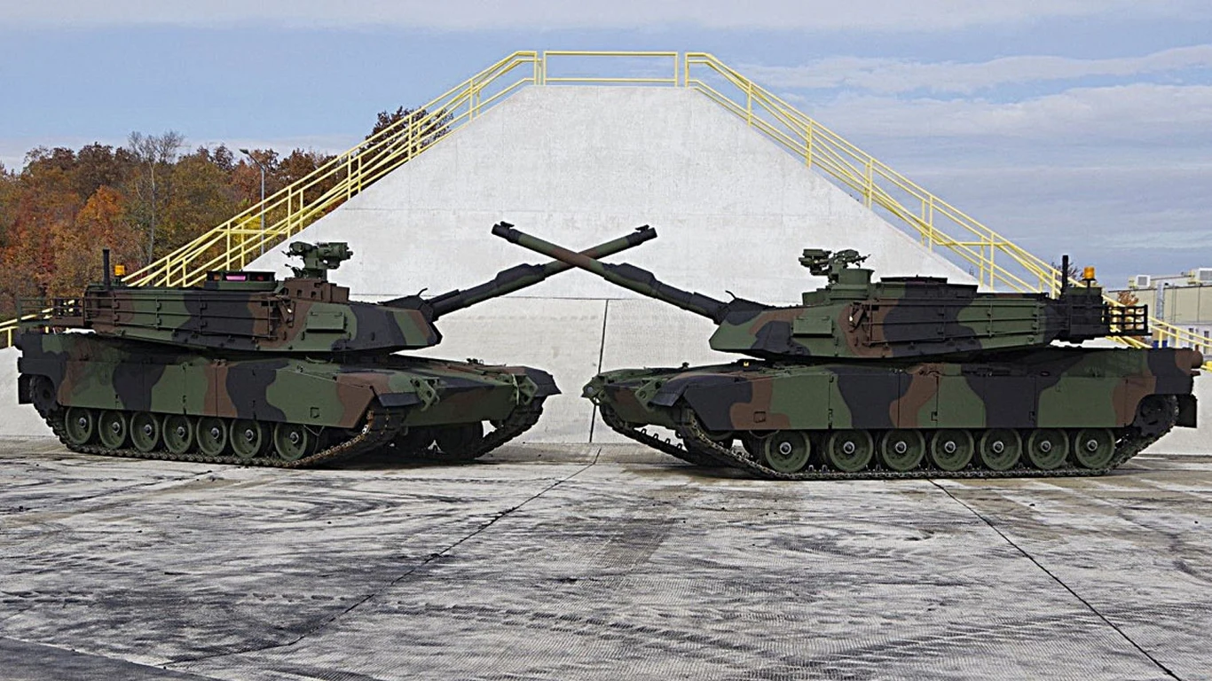 Polskie Abramsy M1A2 SEPv3 Dwa czołgi ustawione naprzeciw siebie z lufami skrzyżowanymi na tle betonowej rampy z żółtymi barierkami, w tle widoczna jesienna roślinność.