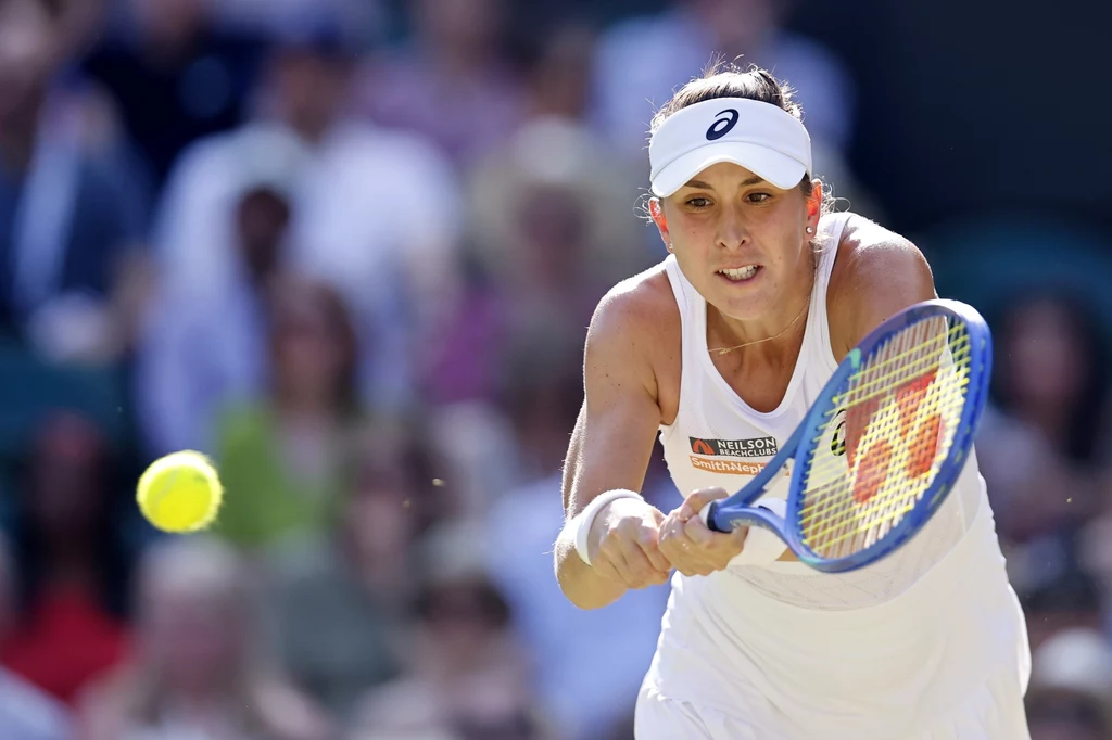 Belinda Bencic Zawodniczka w białym stroju sportowym skupiona podczas odbicia piłki tenisowej, trzymająca rakietę tuż przed kontaktem z piłką; w tle widoczni rozmyci kibice na trybunach.