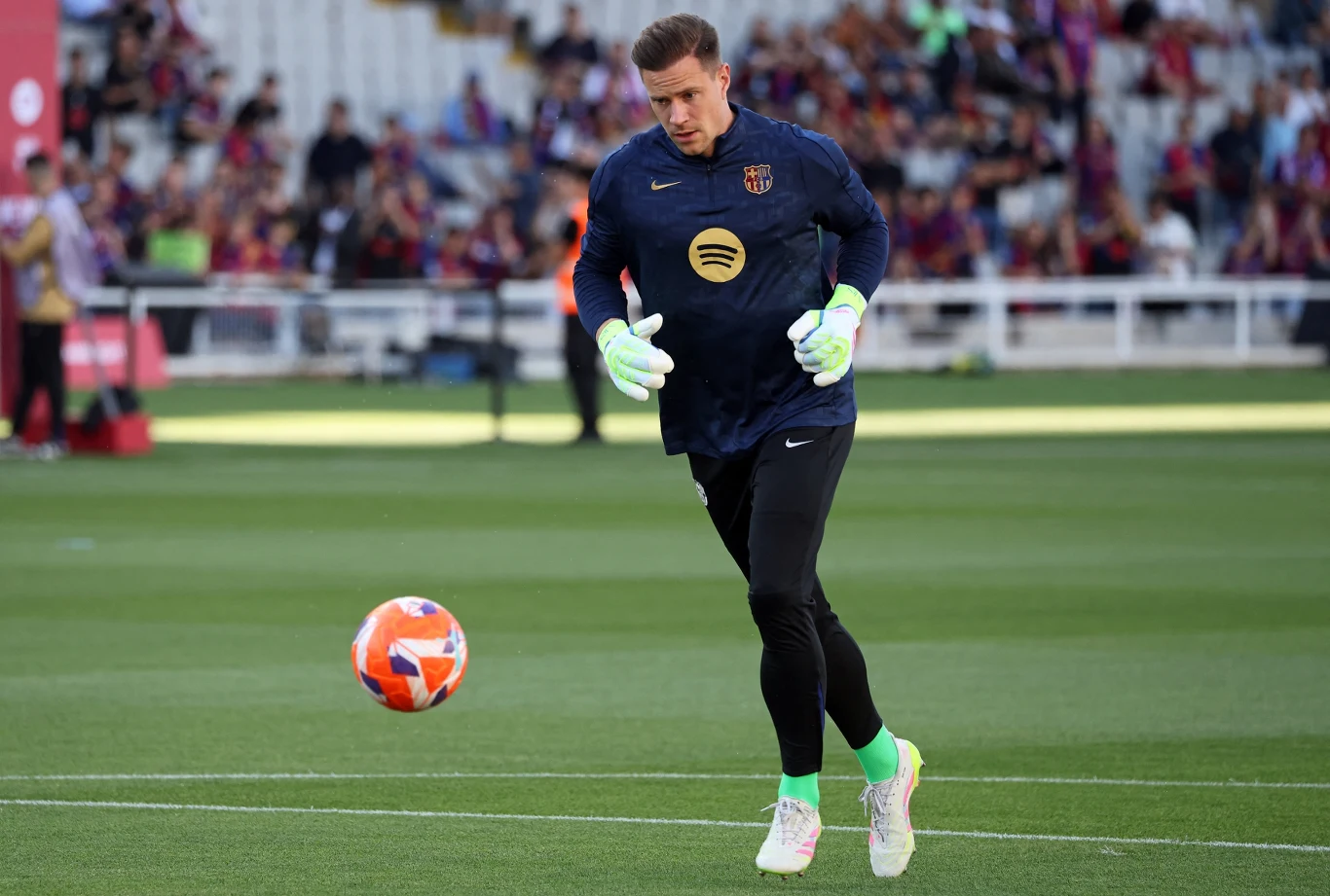 Bramkarz w stroju treningowym FC Barcelona przygotowuje się do gry na murawie stadionu, w tle widoczna rozmyta publiczność oraz trybuny.