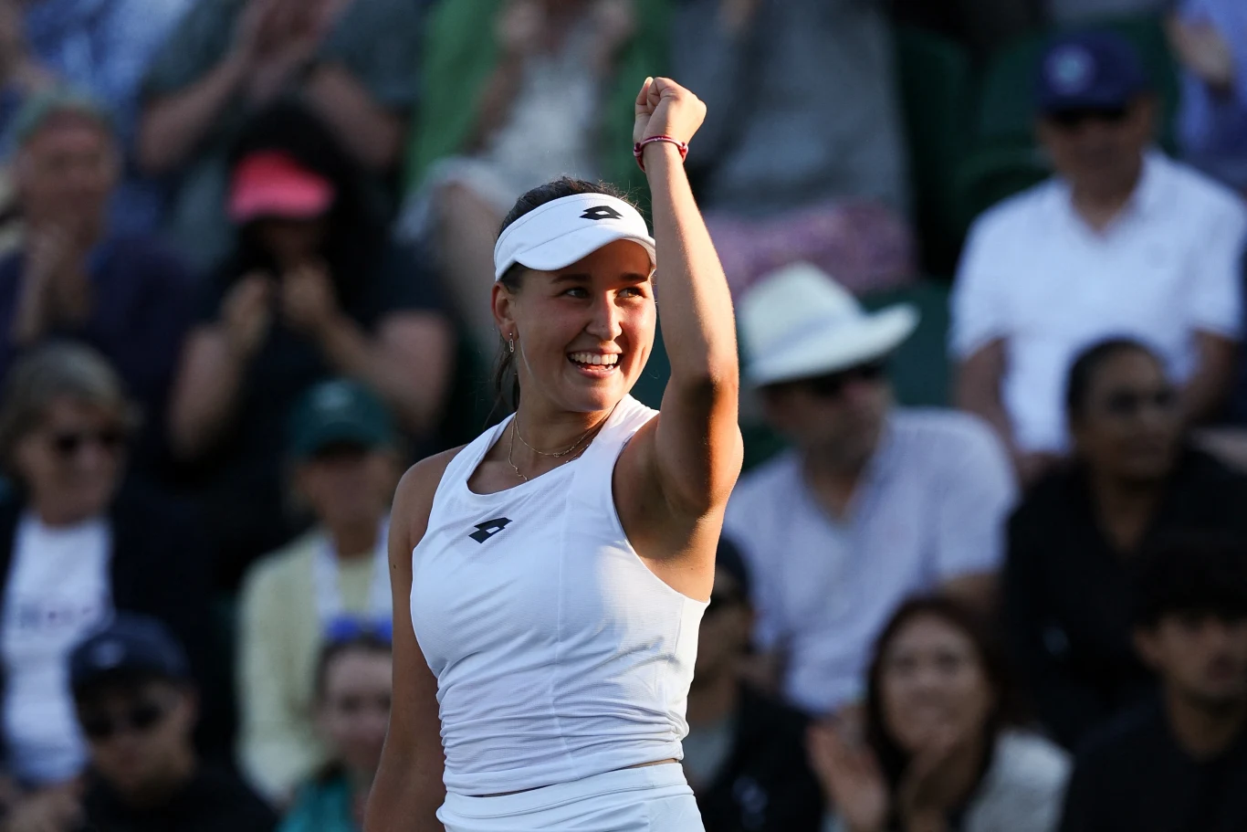 Kamilla Rachimowa Tenisistka ubrana w biały sportowy strój z opaską na głowie unosi zaciśniętą pięść w geście triumfu, na trybunach widoczna grupa kibiców obserwujących mecz.