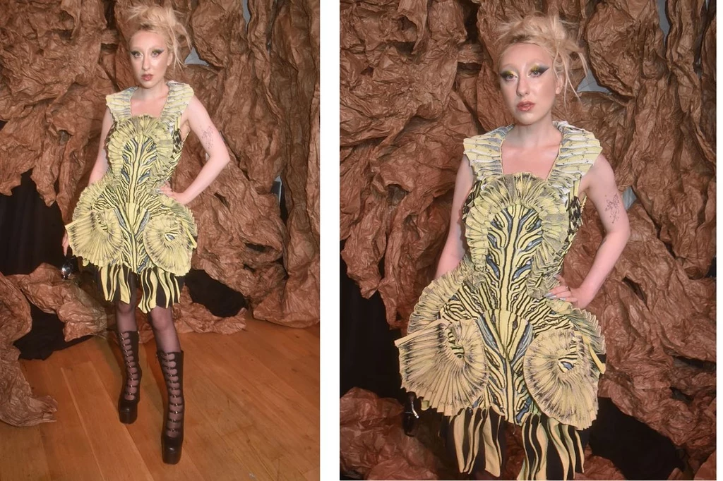 Luna podczas Paris Fashion Week Kobieta w oryginalnej sukience inspirowanej wzorami zwierzęcymi, stojąca na tle brązowej, teksturowanej dekoracji przypominającej faunę lub skorupę drzewa, w butach na wysokim obcasie i ekstrawaganckim makijażu.