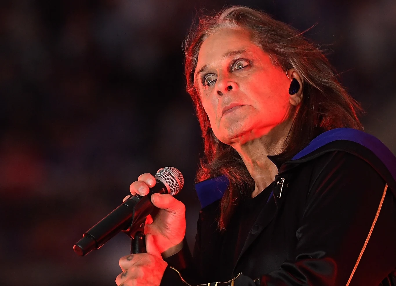 Ozzy Osbourne zaangażował się w nietypową akcję charytatywną Mężczyzna trzyma mikrofon podczas występu scenicznego, oświetlony intensywnym czerwonym światłem, z wyrazistym makijażem oczu i ekspresyjnym wyrazem twarzy.