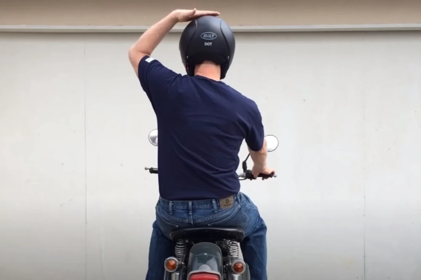 Poklepywanie się po kasku oznacza patrol policji w pobliżu / screen: Youtube Mężczyzna w kasku motocyklowym siedzi na motocyklu, trzymając jedną rękę na głowie, ubrany w granatową koszulkę i dżinsy, tylna część pojazdu oraz sygnalizatory świetlne są dobrze widoczne.