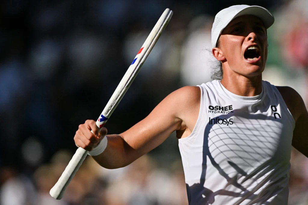 Iga Świątek na Wimbledonie 2025 Tenisistka w białym stroju sportowym trzyma rakietę tenisową i wyraża silne emocje, prawdopodobnie po wygranym punkcie podczas meczu na korcie, tło rozmyte z widoczną publicznością.