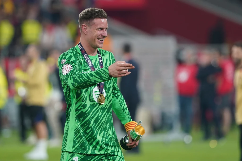 Marc-Andre ter Stegen Bramkarz ubrany w zielony strój z medalem na szyi świętuje na stadionie, trzymając złotą statuetkę oraz opaskę kapitana, zadowolony po wygranym meczu finałowym.