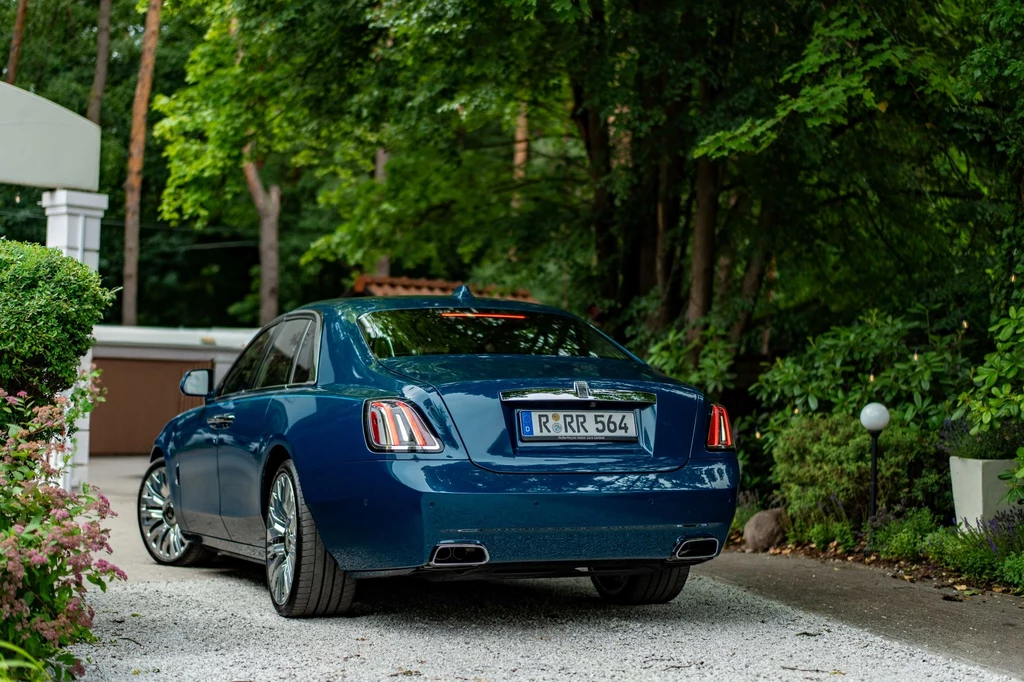 Rolls-Royce Ghost drugiej generacji zadebiutował w 2020 roku. Został stworzony w ramach filozofii "Post Opulent" odrzucającą "powierzchowne przejawy bogactwa". Luksusowy niebieski samochód osobowy zaparkowany na żwirowej alejce prowadzącej do eleganckiego domu otoczonego bujną zielenią ogrodu.