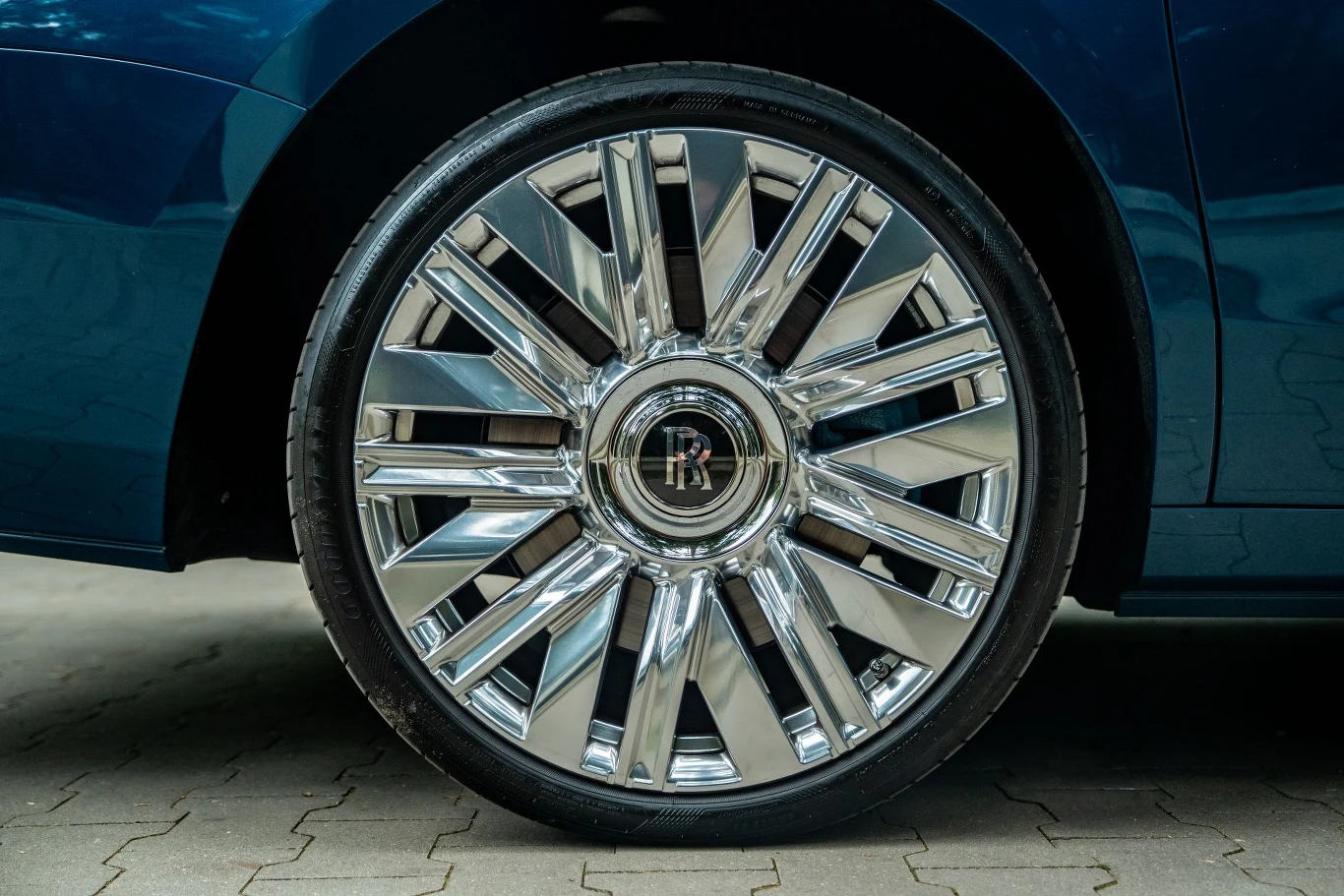 Chromowana felga z logo Rolls-Royce, zamontowana na luksusowym niebieskim samochodzie, detale koła odbijają otoczenie.