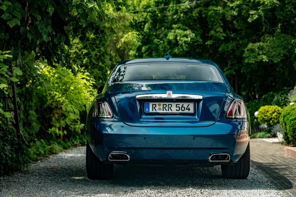 W ramach modernizacji z 2024 roku z tyłu zmieniono tylko światła. Nowe zostały zainspirowane tymi znanymi z modelu Spectre. Tył luksusowego, niebieskiego samochodu marki Rolls-Royce zaparkowanego na żwirowej alejce otoczonej gęstą zielenią i ogrodową roślinnością.
