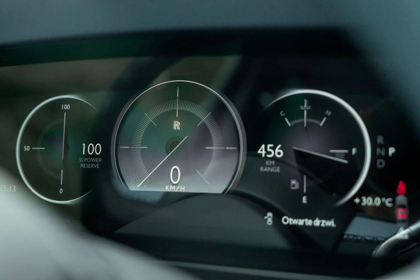 Cyfrowy panel wskaźników samochodu Rolls-Royce z widocznymi licznikami prędkości, rezerwy mocy, poziomu paliwa oraz zasięgu, przy temperaturze zewnętrznej wynoszącej 30°C i komunikatem o otwartych drzwiach.
