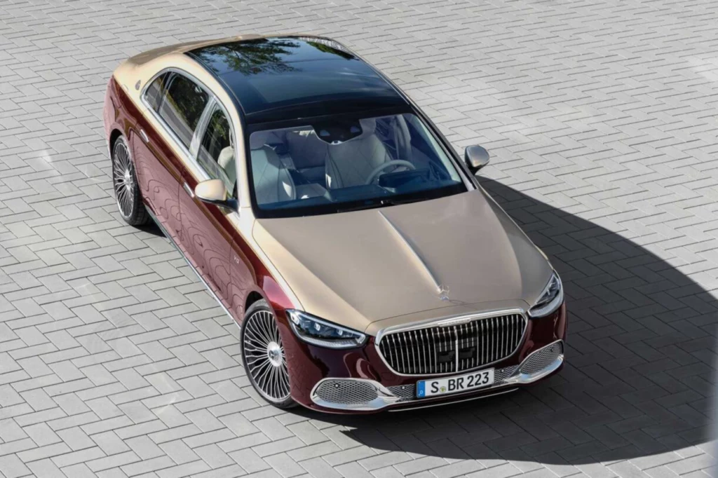 Maybach S680 napędzany jest silnikiem V12 o mocy 612 KM. Ceny rozpoczynają się od 979 900 zł. Dwukolorowy luksusowy sedan Mercedes-Maybach w odcieniach złota i bordo z dużą, chromowaną osłoną chłodnicy, nowoczesnymi reflektorami oraz panoramicznym dachem, zaparkowany na brukowanej powierzchni.