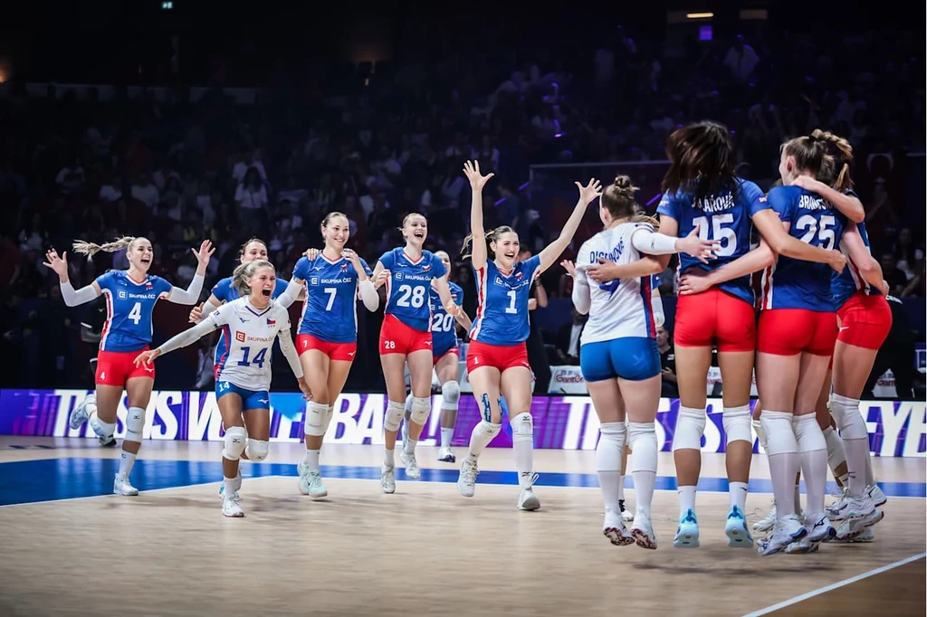 Czeskie siatkarki świętujące zwycięstwo nad reprezentacją Turcji Grupa siatkarek ubranych w sportowe stroje świętuje na boisku, część zawodniczek skacze z radości z uniesionymi rękami, pozostałe obejmują się tworząc zwarty krąg, w tle ciemna widownia.