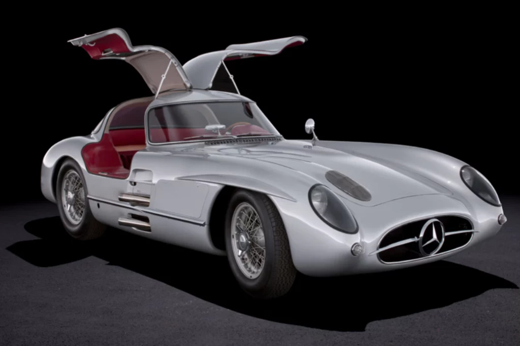 Mercedes 300 SLR Uhlenhaut wyprzedził swoje czasy na każdym kroku. Srebrny, klasyczny samochód sportowy z otwartymi drzwiami typu gullwing i czerwonym wnętrzem, na czarnym tle.