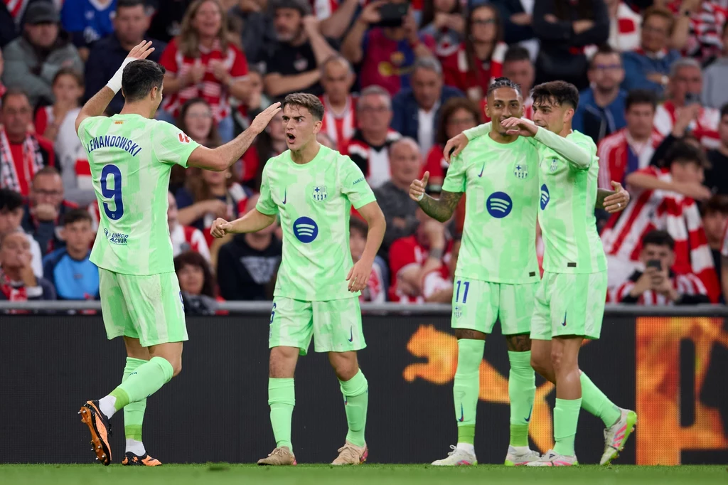 Piłkarze Barcelony Piłkarze drużyny FC Barcelona w jasnozielonych strojach świętują zdobycie gola podczas meczu piłkarskiego, na trybunach widoczna publiczność kibicująca obu drużynom.