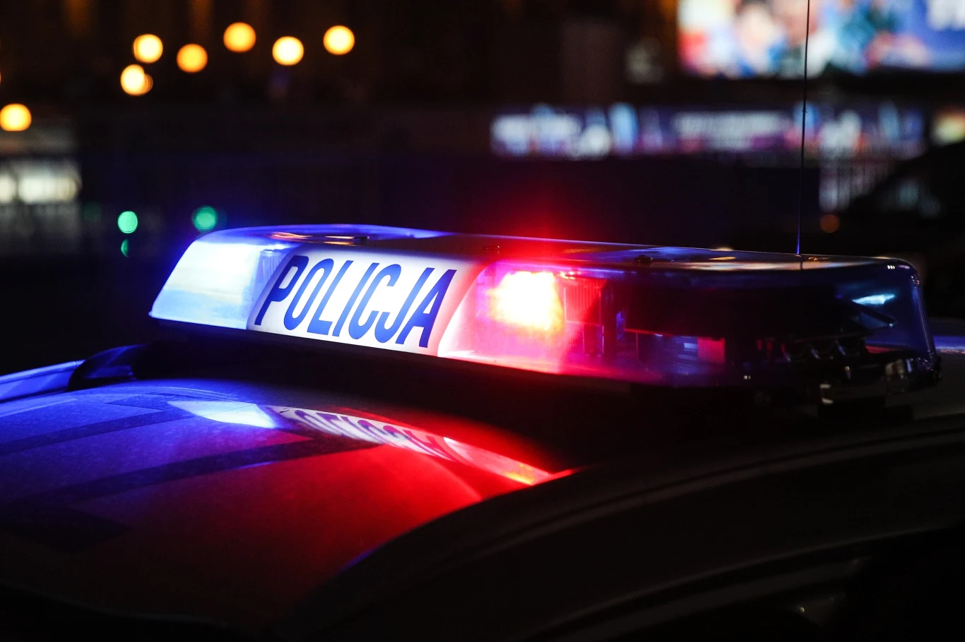 Jest decyzja o areszcie dla podejrzanych ws. wypadku na Wisłostradzie Niebiesko-czerwone światła policyjne na dachu radiowozu z napisem 'Policja', rozświetlone nocne tło miasta w tle.