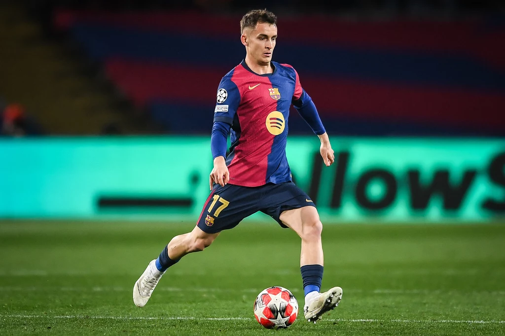Marc Casado Piłkarz w stroju FC Barcelony prowadzi piłkę na murawie stadionu podczas meczu, skupiony i dynamiczny, w tle widoczne rozmyte trybuny i jasne światła reklamowe.