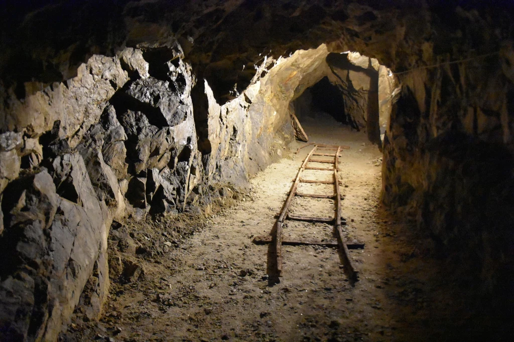 Sieć podziemnych tuneli pod zamkiem Książ skrywa mnóstwo tajemnic i przyciąga poszukiwaczy legendarnego Złotego Pociągu Kamienny tunel kopalni oświetlony sztucznym światłem, przebiegający po torach kolejowych używanych do transportu urobku.