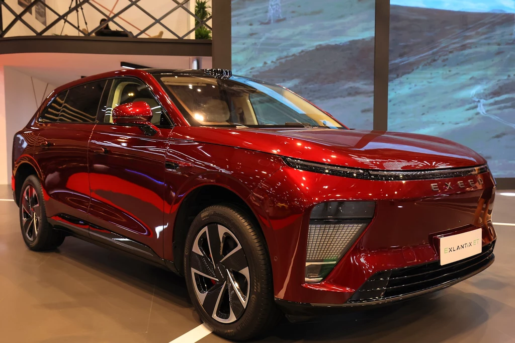 Exlantix ET to SUV dzielący rozwiązania techniczne z modelem ES Nowoczesny, czerwony SUV marki Exeed zaparkowany w salonie wystawowym, z widocznym reflektorem LED, chromowanymi detalami oraz charakterystycznym, aerodynamicznym kształtem nadwozia.