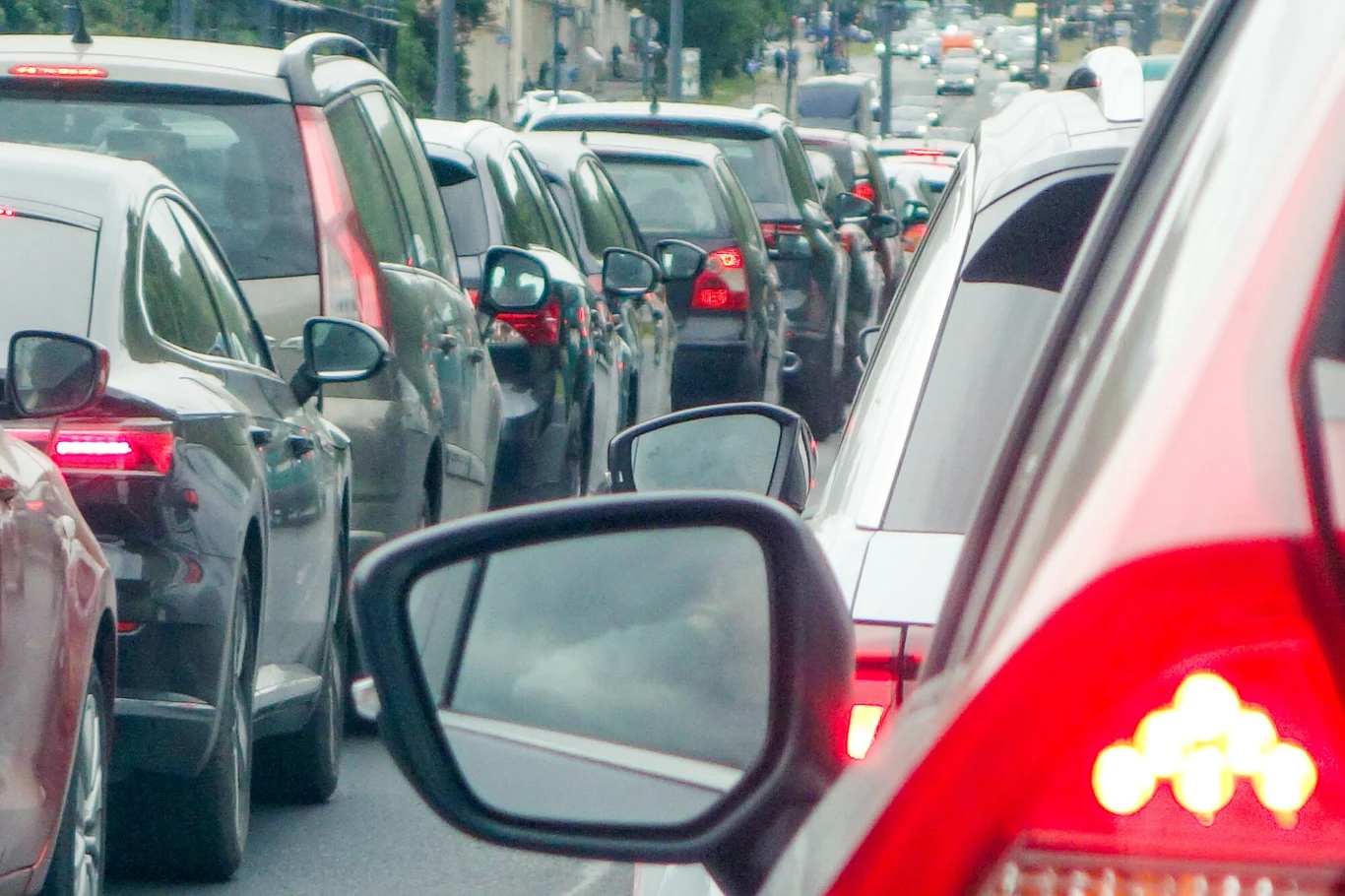 Eksploatacja miejska, częste ruszanie i krótkie trasy są wyniszczające dla silnika Rząd samochodów stojących w miejskim korku, lusterka boczne oraz tylne światła kilku pojazdów, fragmenty ulicy i budynków w tle.