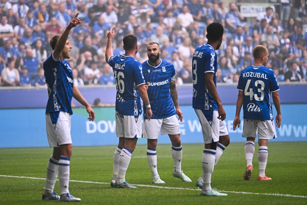 Lech Poznań Pięciu piłkarzy w niebieskich koszulkach na murawie stadionu, otoczonych tłumem kibiców na trybunach, część z nich gestykuluje i rozmawia.