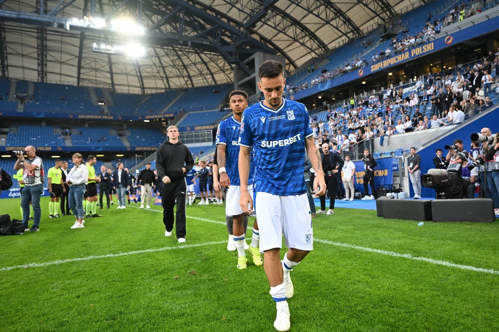 Afonso Sousa, za nim Bryan Fiabema Piłkarze drużyny w niebieskich koszulkach schodzą z boiska na stadionie, wokół obecni są kibice oraz członkowie zespołu, a trybuny zapełnione są widzami.
