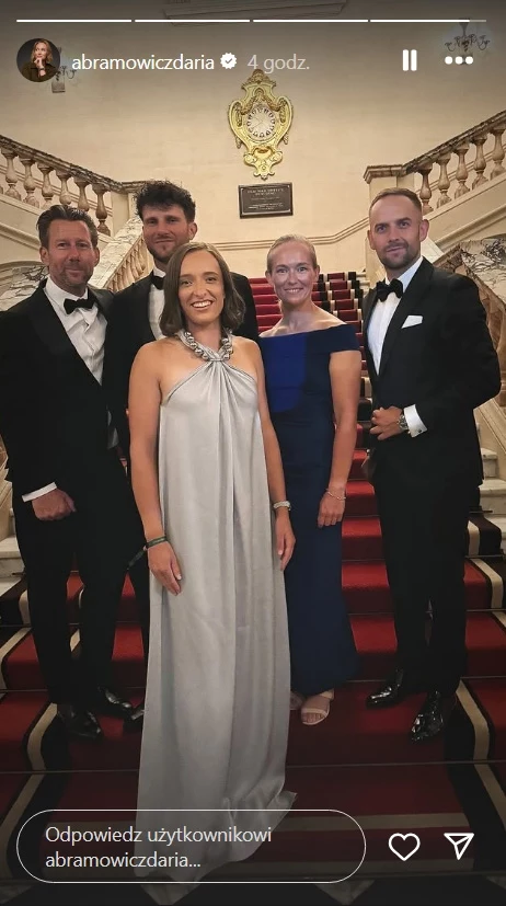 Iga Świątek ze sztabem na balu mistrzów Wimbledonu Pięć elegancko ubranych osób pozuje na czerwonym dywanie na marmurowych schodach w reprezentacyjnym wnętrzu; dwie kobiety w długich sukniach oraz trzech mężczyzn w smokingach, w tle ozdobna balustrada i herb na ścianie.