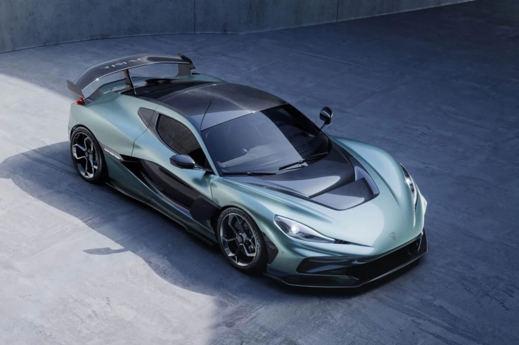 Sprint od 0 do 400 km/h zajmuje temu elektrycznemu hipersamochodowi 17,35 sekundy. Sportowy samochód w metalicznym, zielonym kolorze z czarnymi akcentami, szerokimi kołami i dużym tylnym spojlerem, zaparkowany na betonowym podłożu w industrialnym otoczeniu.