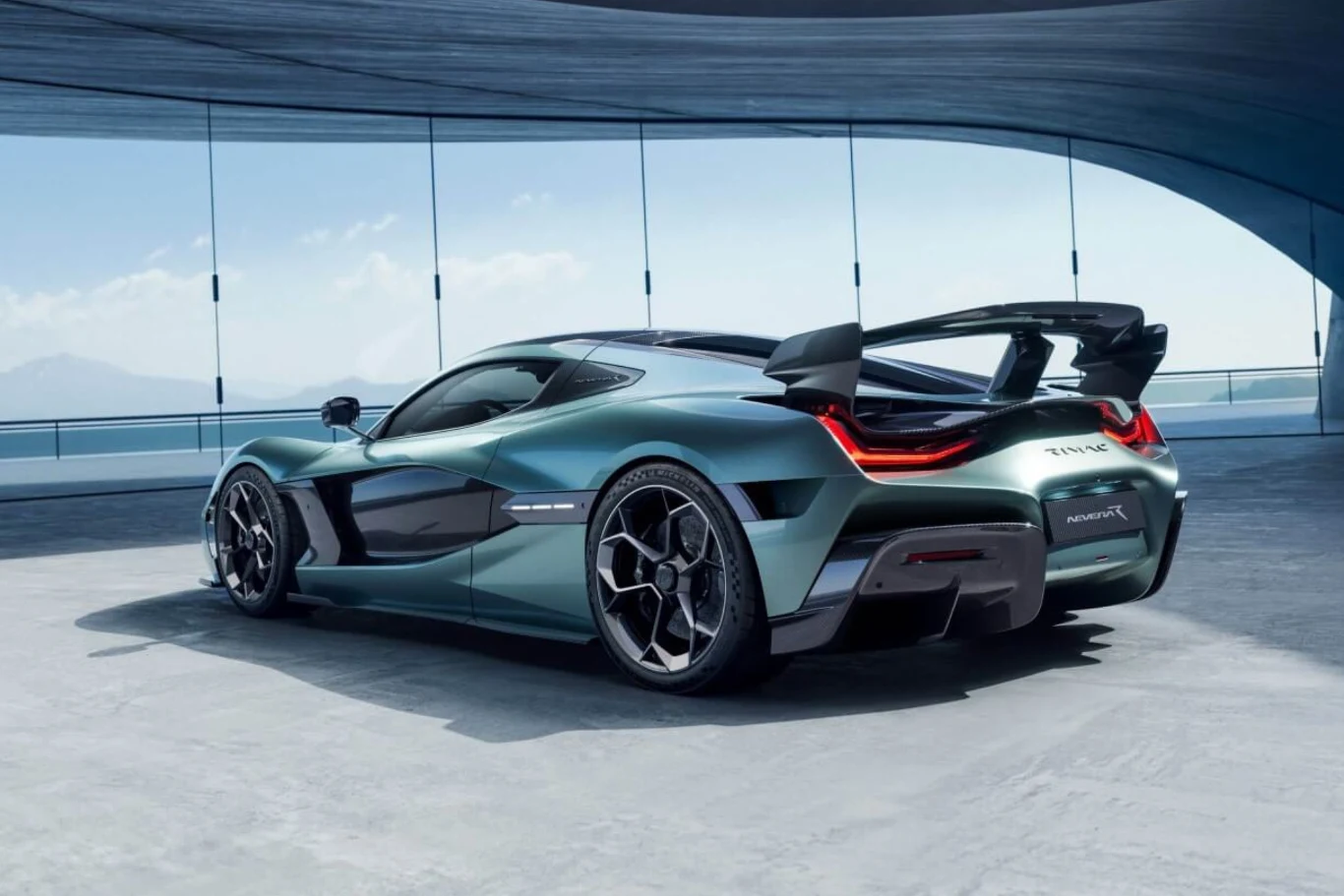 Zielony supersamochód Rimac Nevera z wyrazistymi liniami, dużym tylnym spoilerem i reflektorami LED zaparkowany w nowoczesnym, przeszklonym garażu z widokiem na góry i jezioro.