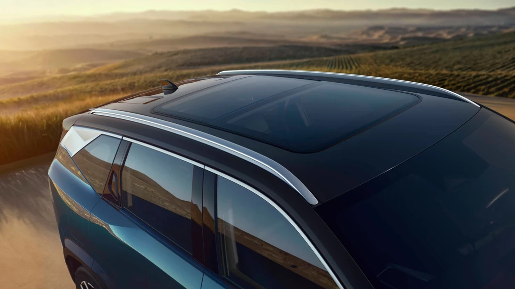 SUV oferuje panoramiczny dach. Szklany dach panoramiczny samochodu terenowego błyszczący w promieniach zachodzącego słońca, w tle rozciągające się pola i wzgórza.