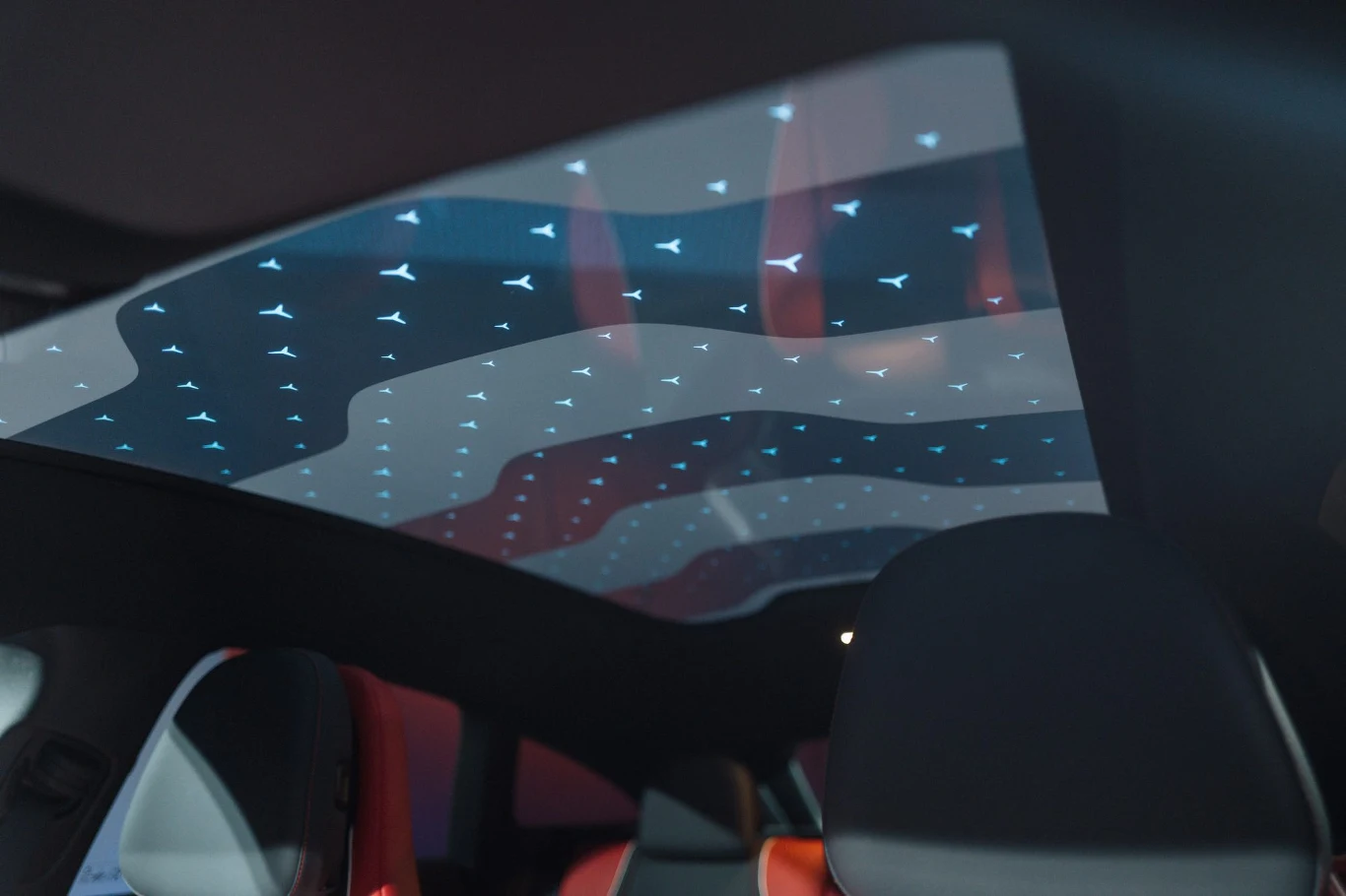 Pasażerowie decydują, czy dach ma być przezroczysty, czy "mleczny" Panoramiczny dach samochodu wyposażony w efektowne podświetlenie LED w formie małych symboli, widoczne przednie fotele z czarnym i czerwonym wykończeniem.