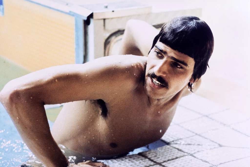Mark Spitz w czasie igrzysk olimpijskich w Monachium (1972) Mężczyzna z wąsem i krótkimi ciemnymi włosami wyłania się z basenu, opierając się ręką o brzeg, ma na sobie tylko kąpielówki, w tle fragment niecki basenowej.