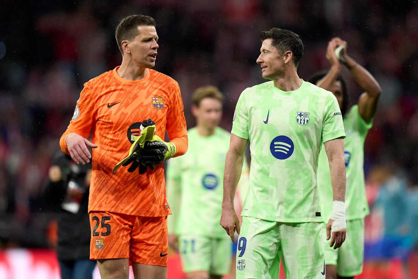 Wojciech Szczęsny i Robert Lewandowski Dwaj piłkarze w sportowych strojach rozmawiają na boisku po zakończonym meczu, w tle rozmazani kibice i inni zawodnicy.