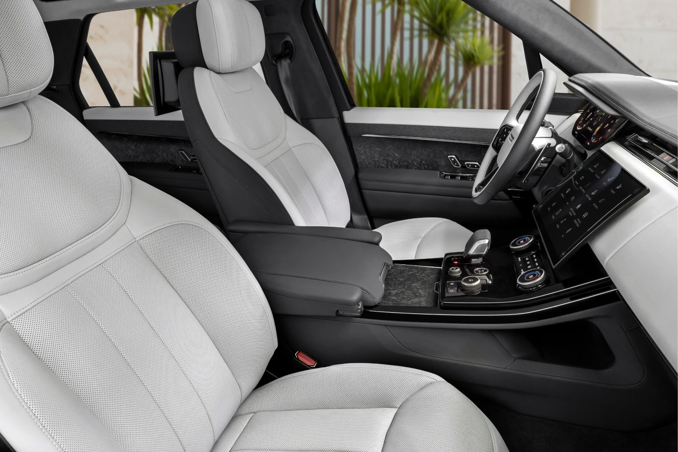 Luksusowe wnętrze samochodu z białymi, skórzanymi fotelami, nowoczesną konsolą centralną z przyciskami i wyświetlaczami oraz widocznymi elementami deski rozdzielczej.