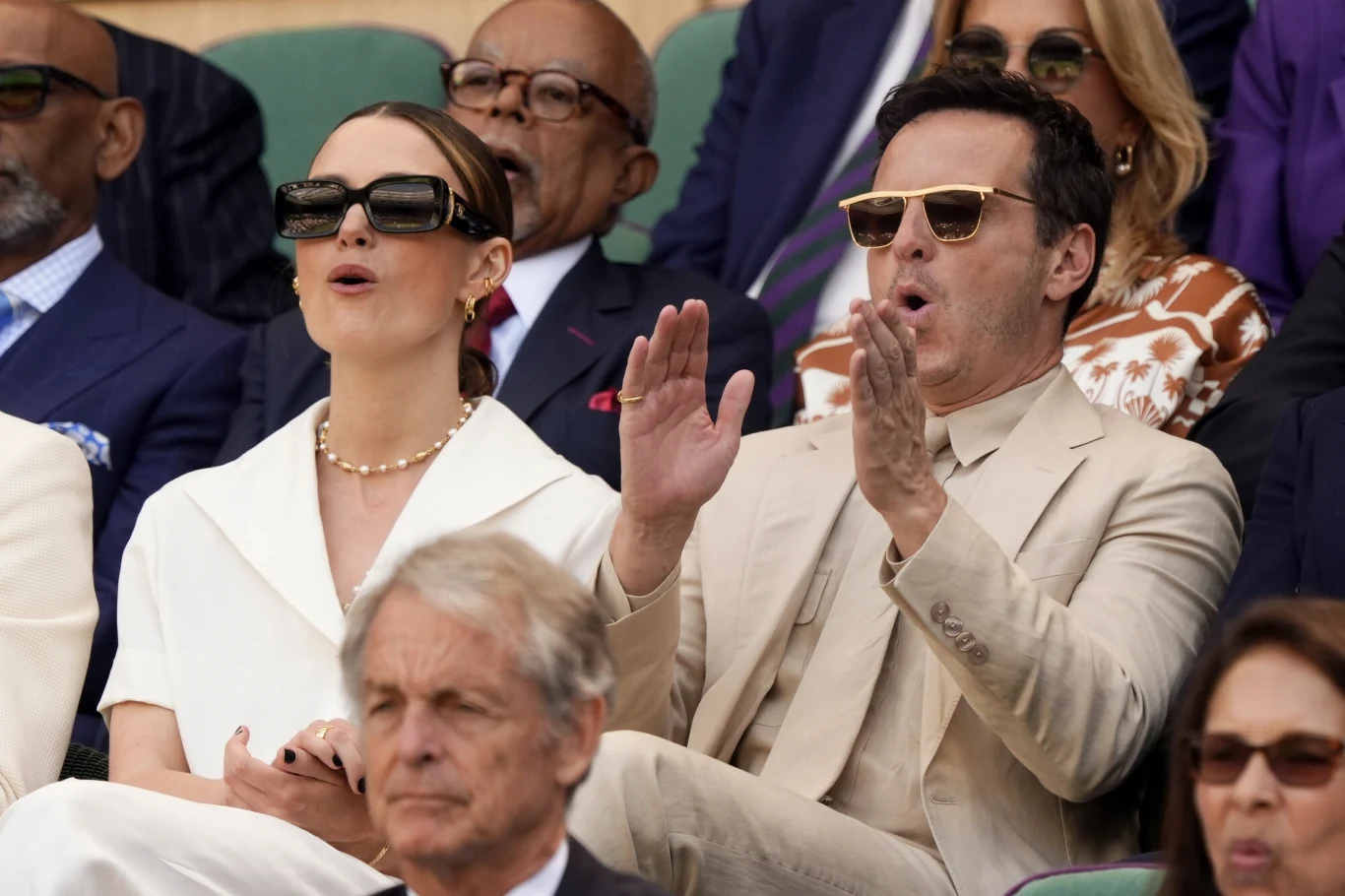 Keira Knightley i Andrew Scott na Wimbledonie Grupa elegancko ubranych osób siedzi na trybunach, dwoje z nich, mężczyzna i kobieta w okularach przeciwsłonecznych, reagują emocjonalnie, bijąc brawo i wyrażając podziw.