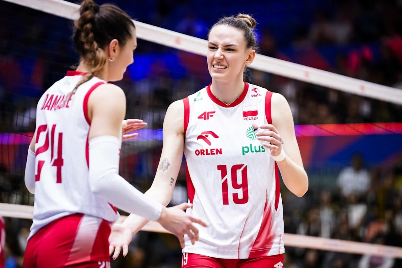 Polskie siatkarki szykują się do walki o medal Ligi Narodów Dwie siatkarki reprezentacji Polski w trakcie meczu, ubrane w oficjalne stroje sportowe, wymieniające się gestami i emocjami na boisku, w tle widoczne siatka i rozmyta publiczność.