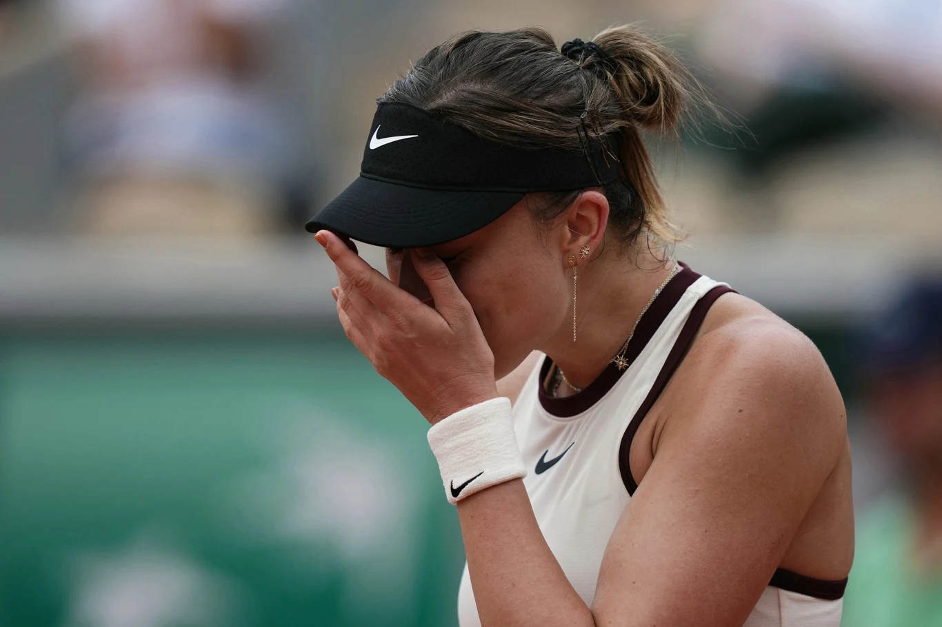 Zawodniczka na korcie tenisowym w sportowym stroju z czapeczką zasłania twarz dłonią, wyraźnie przeżywając emocje po zakończonym meczu.