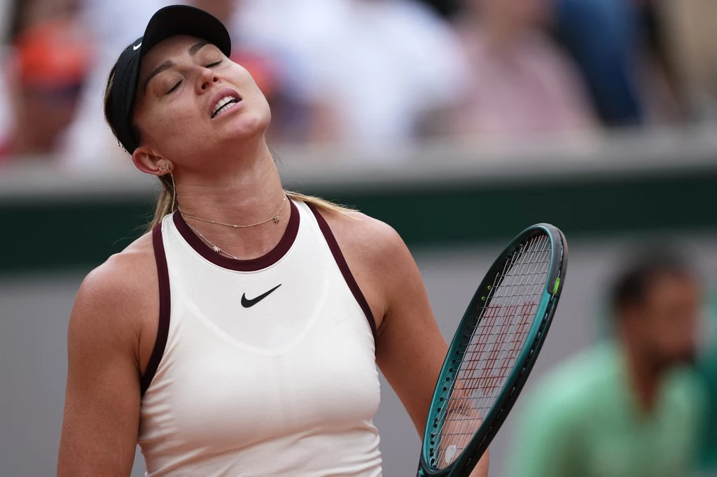 Paula Badosa Zawodniczka tenisowa w sportowym stroju z rakietą w dłoni, z wyrazem frustracji lub zmęczenia na twarzy, lekko odchylając głowę do tyłu, w tle rozmyte sylwetki kibiców na trybunach.