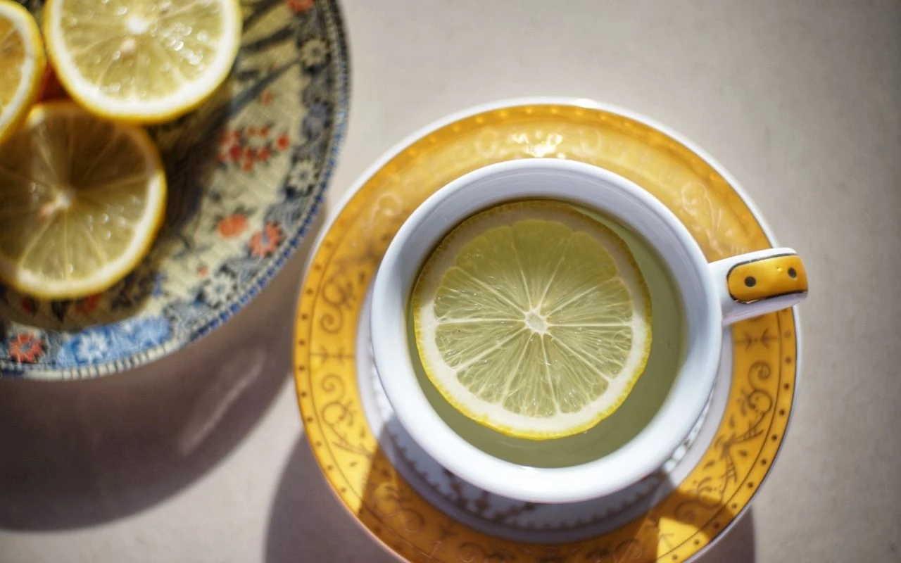 Filiżanka z napojem udekorowanym plasterkiem cytryny oraz talerz z kilkoma plasterkami cytryny, całość utrzymana w ciepłej kolorystyce, światło podkreśla świeżość owoców