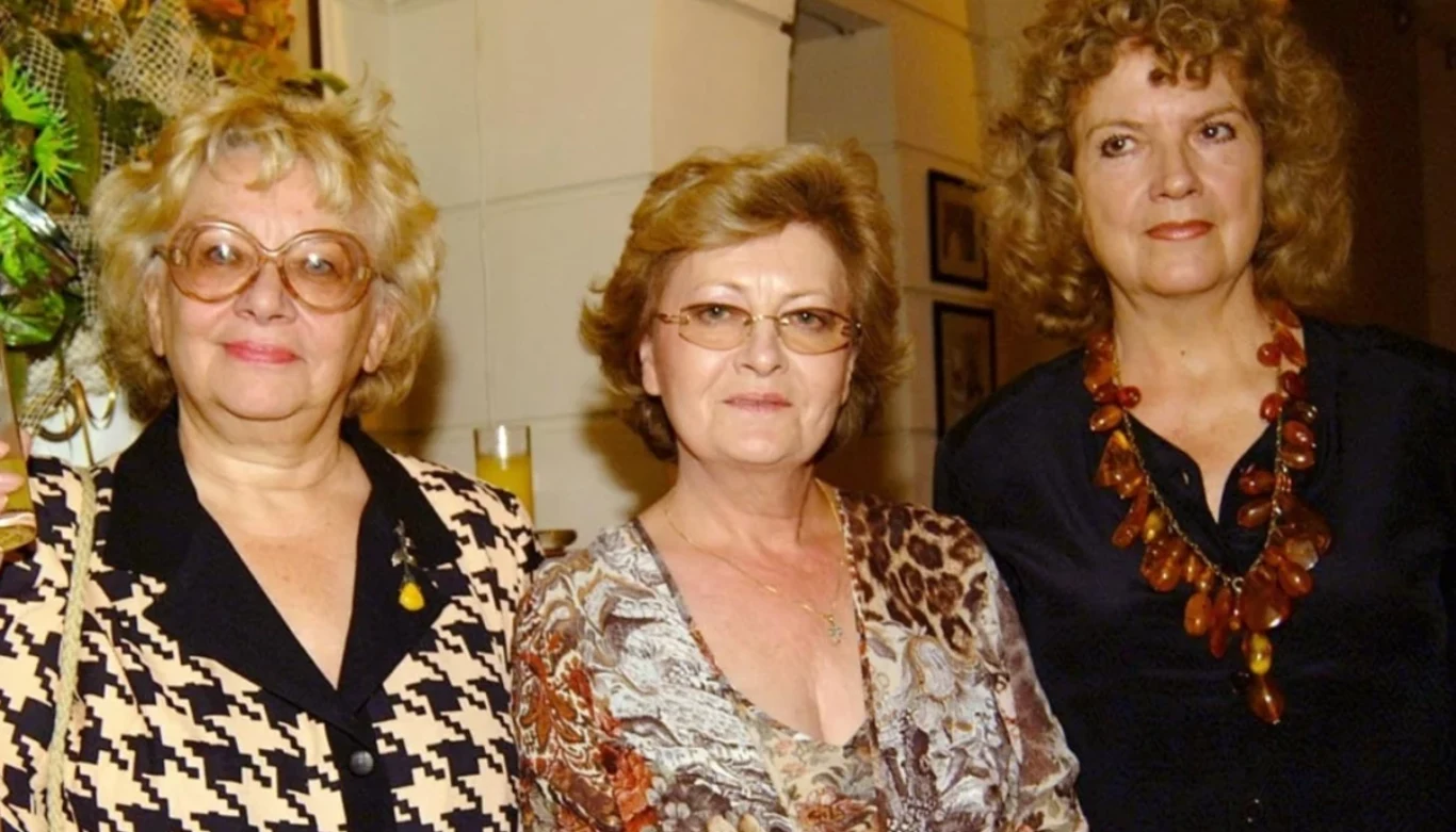 Lucyna Arska, a u jej boku Małgorzata Gorzewska-Cegiełło i Stenia Kozłowska Trzy elegancko ubrane kobiety w średnim wieku stoją obok siebie i patrzą w stronę obiektywu, dwie z nich noszą okulary, jedna ma wyrazisty naszyjnik z bursztynów, a tło sugeruje wnętrze galerii lub miejsca publicznego.