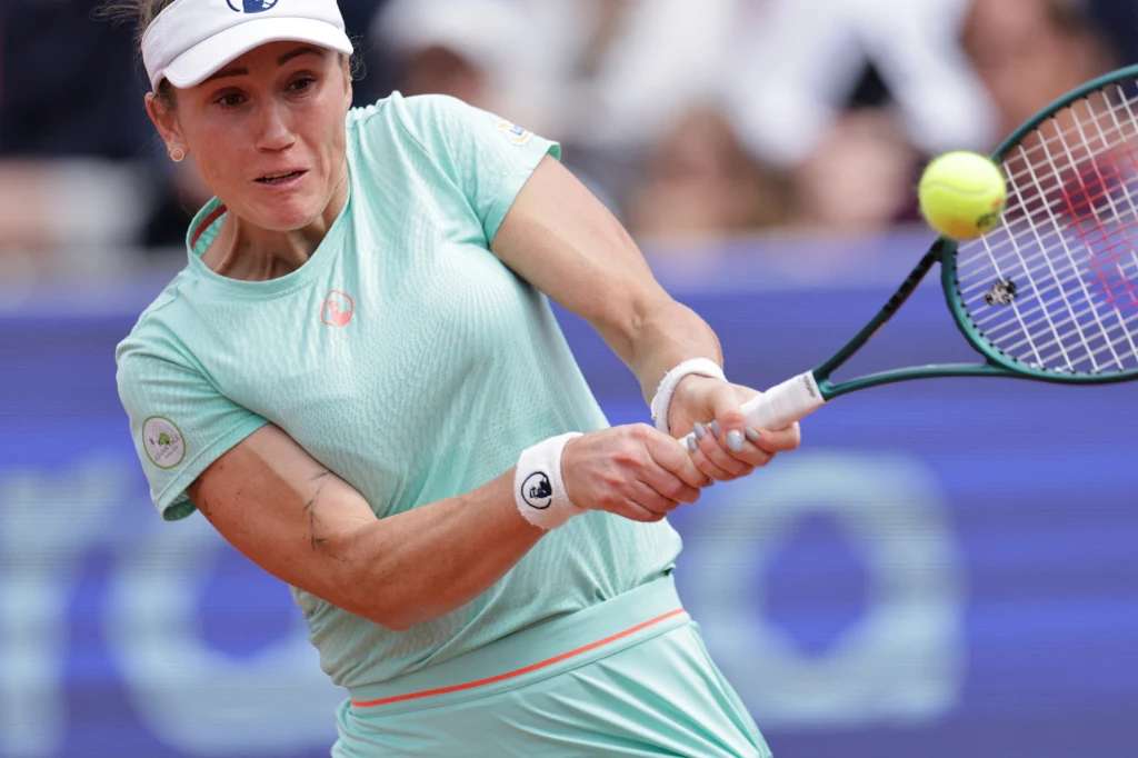 Katarzyna Kawa Tenisistka w jasnoniebieskim stroju wykonuje uderzenie backhandowe podczas meczu tenisowego, koncentrując się na piłce lecącej w jej kierunku, tłum w tle jest rozmyty.