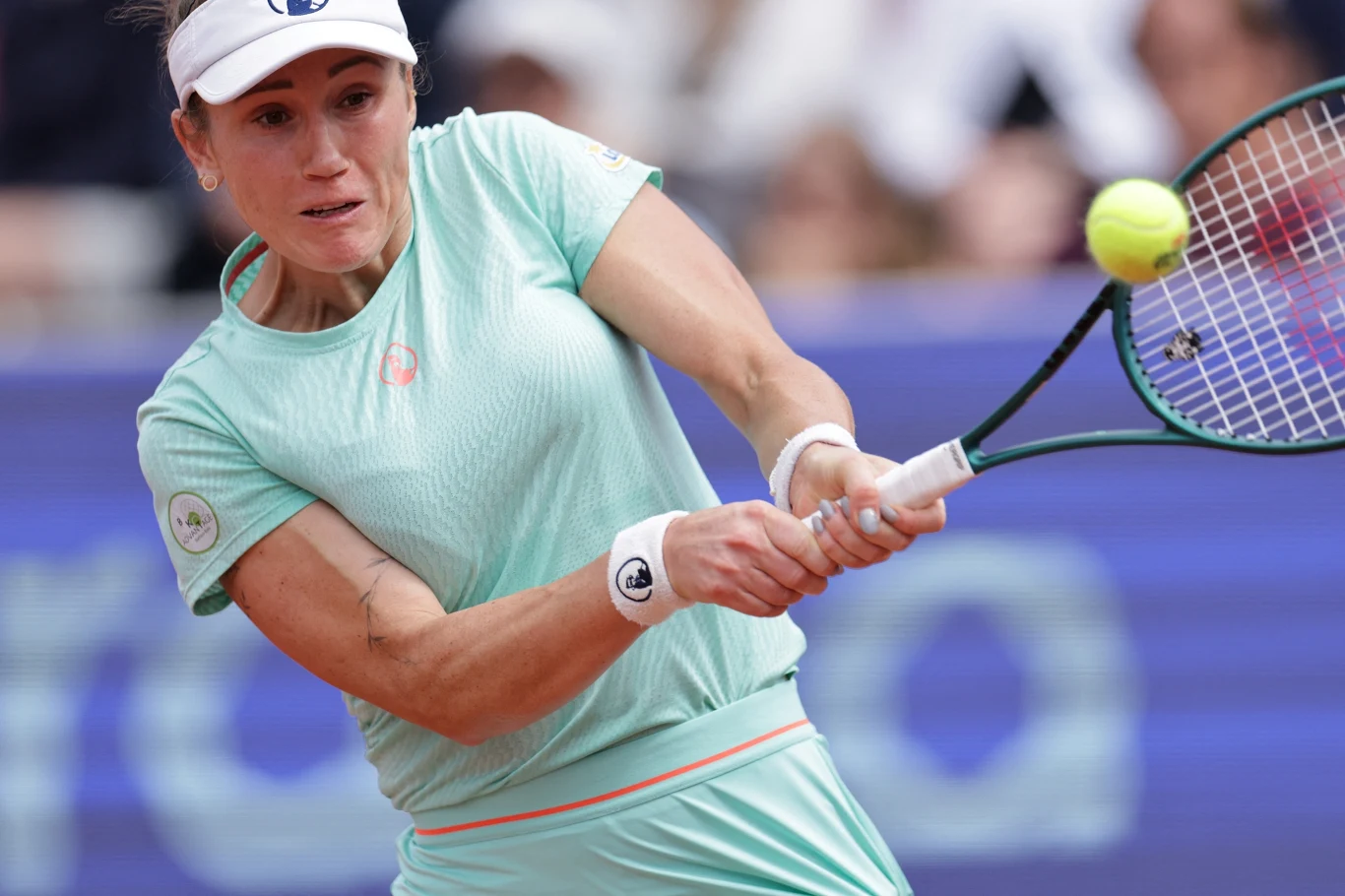 Katarzyna Kawa Tenisistka w jasnoniebieskim stroju wykonuje uderzenie backhandowe podczas meczu tenisowego, koncentrując się na piłce lecącej w jej kierunku, tłum w tle jest rozmyty.