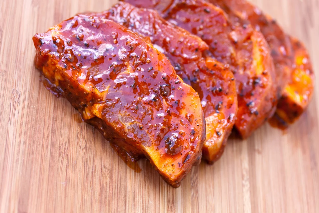Soczysty schab to idealny pomysł na obiad Plastry soczystego pieczonego mięsa w gęstym, aromatycznym sosie barbecue ułożone na drewnianej desce.
