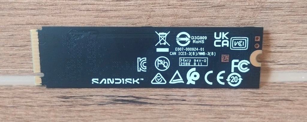 WD_Black SN8100 2TB SSD Dysk SSD SanDisk w formacie M.2 leżący na drewnianej powierzchni, z widocznymi oznaczeniami technicznymi oraz certyfikatami zgodności.