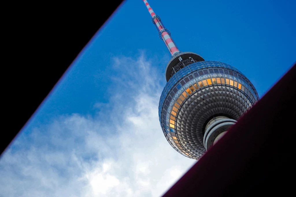 Berlińska Wieża Telewizyjna znajdująca się w berlińskiej dzielnicy Mitte, w pobliżu Alexanderplatz, osiąga wysokości 368 metrów. Fragment Telewizji Berlińskiej z charakterystyczną kulą i anteną na tle niebieskiego nieba, ujęty z nietypowej perspektywy przez ciemne krawędzie.